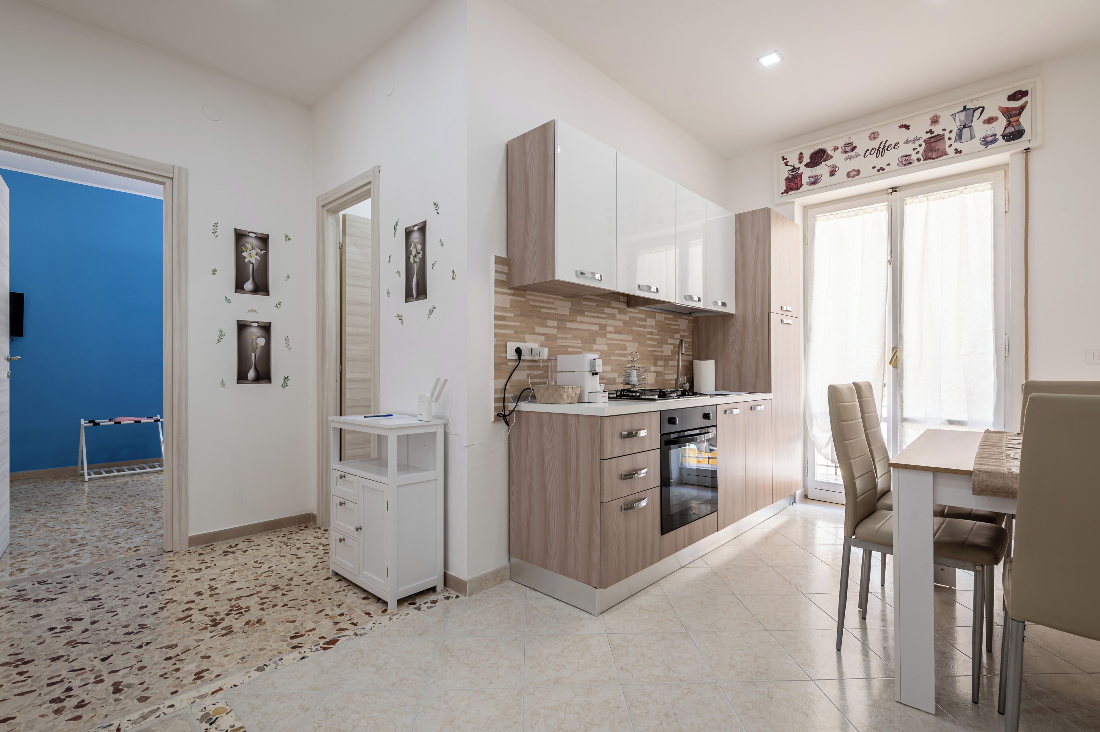 A modern kitchen with white cabinets, a built-in oven, and a dining area with a table and chairs.