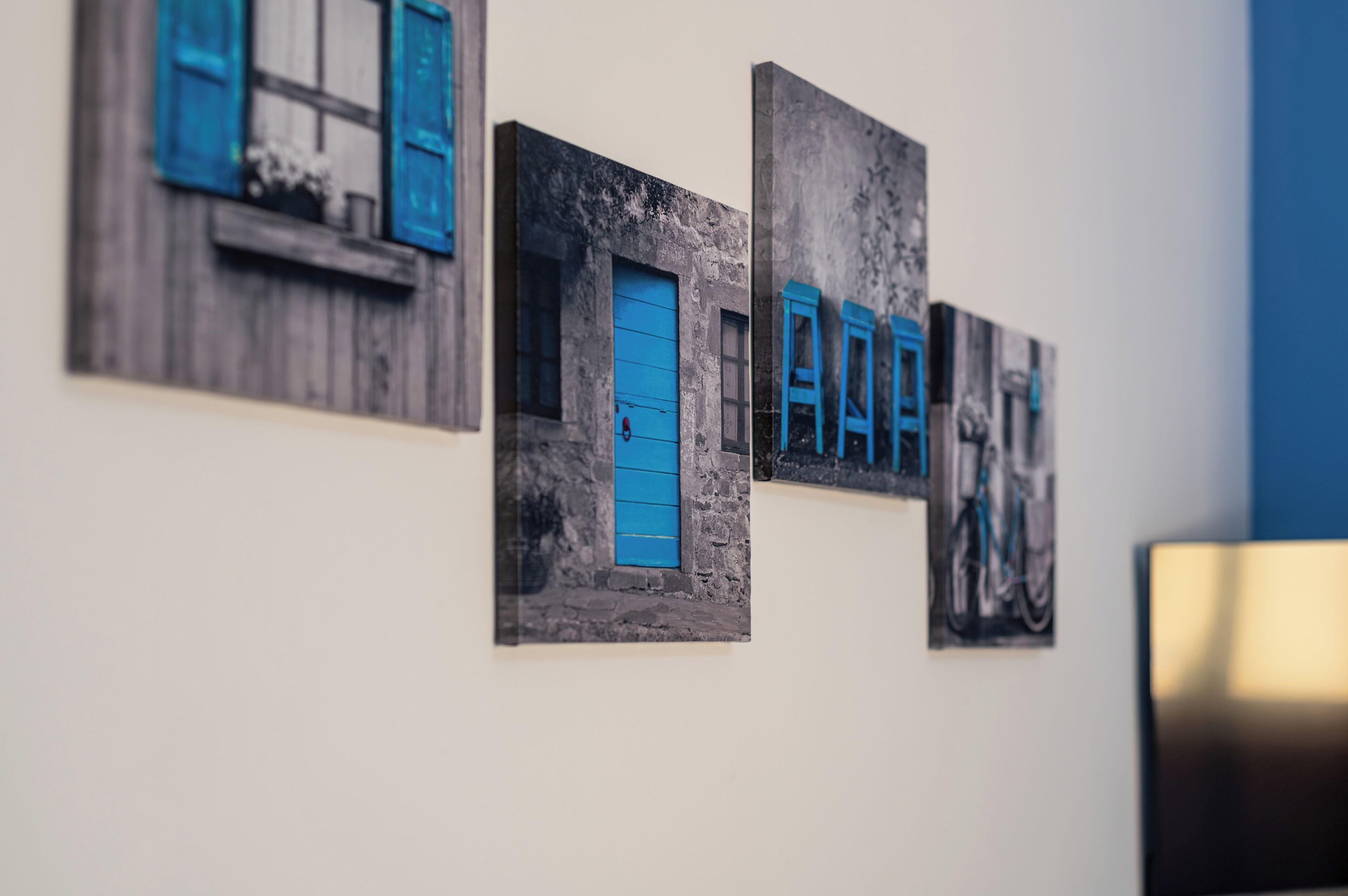 Een muur met drie kunstwerken in lijsten, waarop gebouwen met blauwe deuren en ramen te zien zijn.