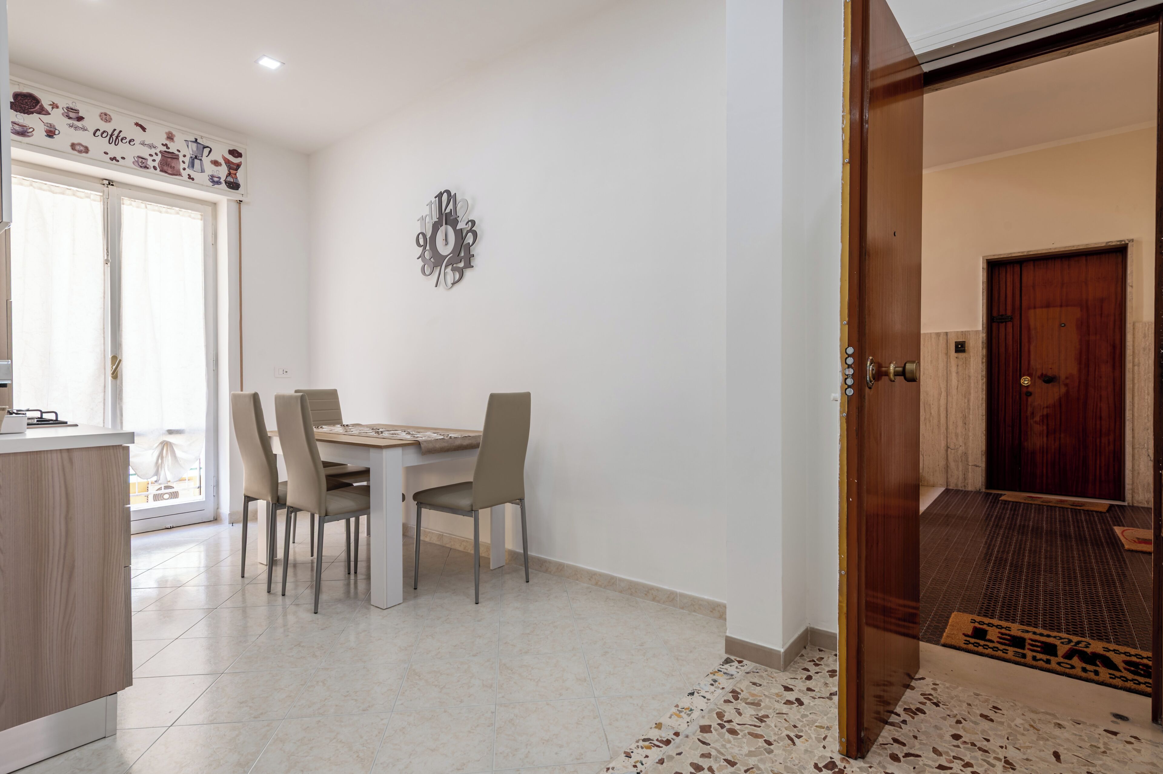 Un comedor con una mesa, sillas, un reloj de pared y una puerta que da a otra habitación.