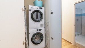 Un lavadero con dos lavadoras apiladas de carga frontal y un box de ducha con mampara de vidrio.