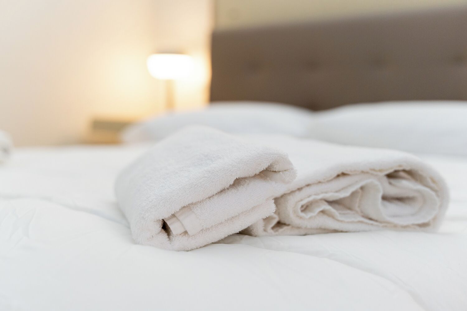 Ein ordentlich gemachtes Bett mit weißen Leinen und einem gefalteten weißen Handtuch.