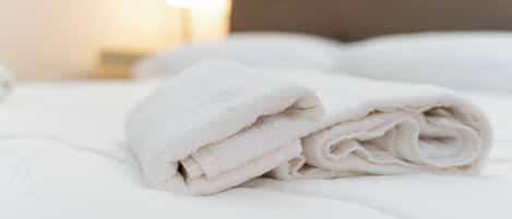 Cama bem arrumada com lençóis brancos e uma toalha branca dobrada por cima.