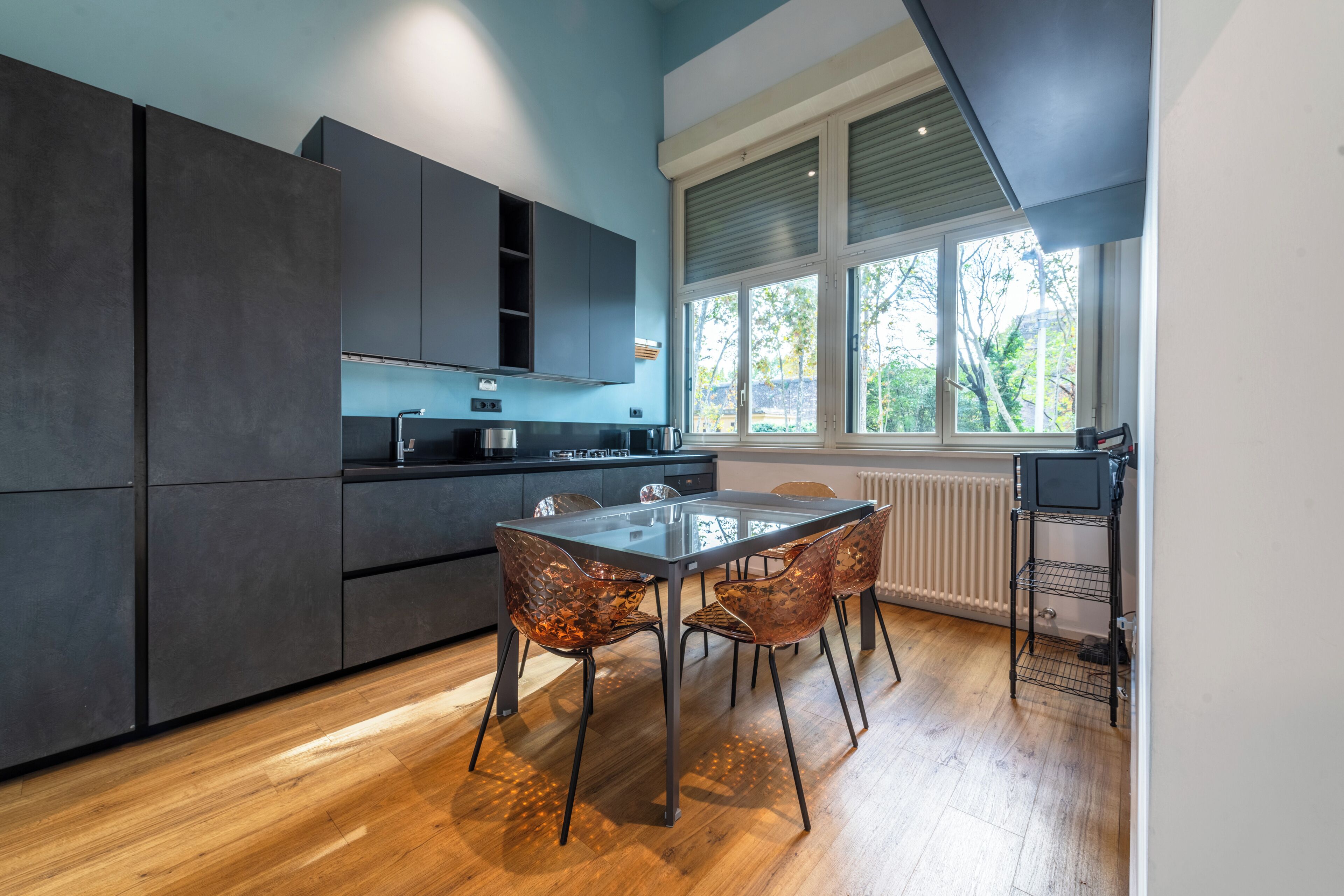 Una cocina moderna con armarios oscuros, una mesa de vidrio y sillas de cobre.