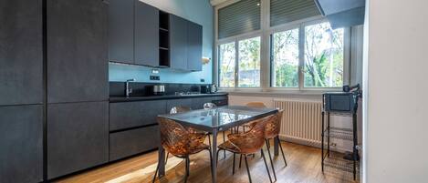 Una cocina moderna con armarios oscuros, una mesa de vidrio y sillas de cobre.