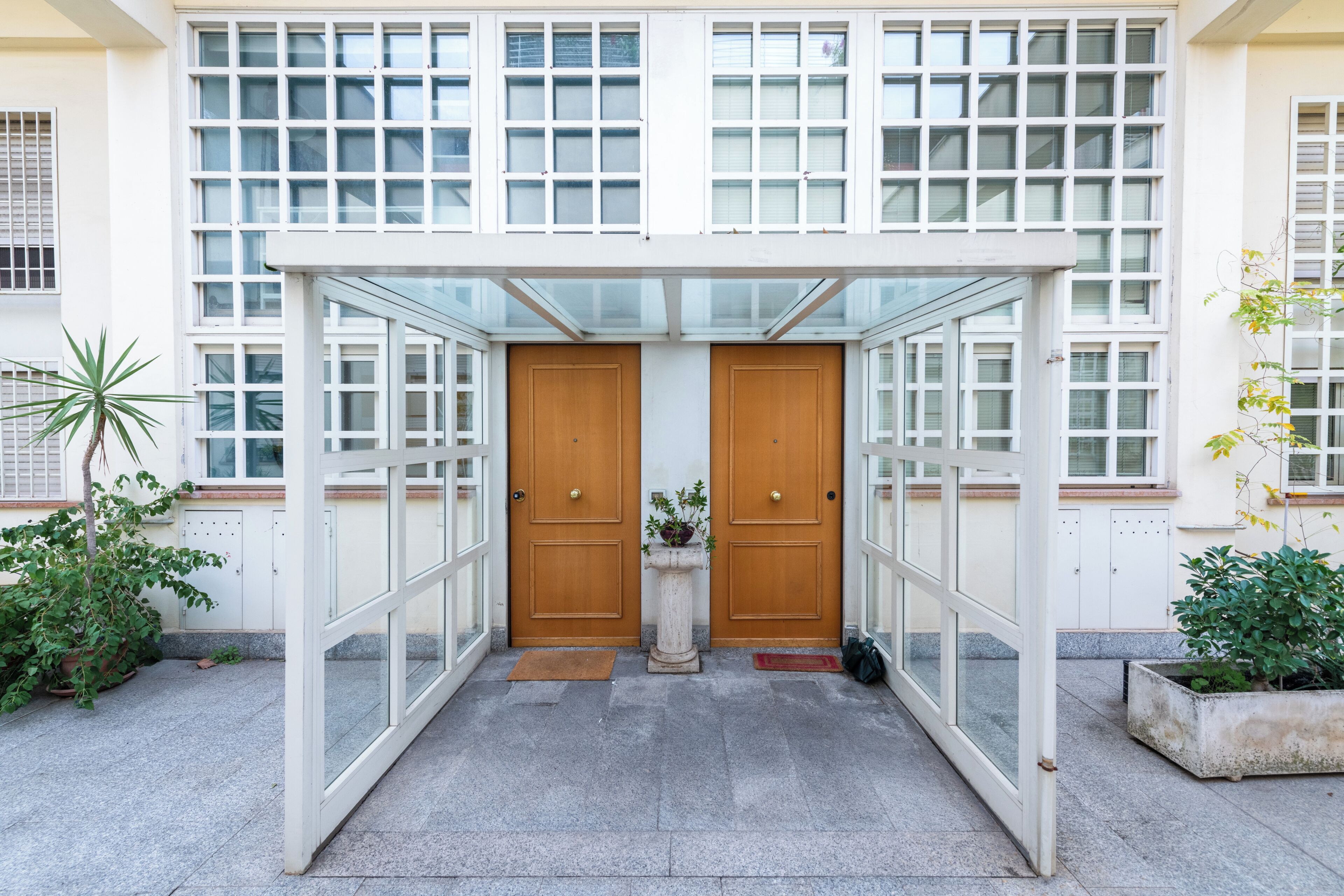 A covered entrance with a glass canopy, two wooden doors, and potted plants.