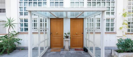 Una entrada cubierta con toldo de vidrio, dos puertas de madera y plantas en macetas.