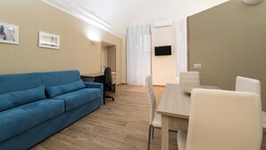 Un salon moderne avec un canapé bleu, une table à manger avec des chaises, un téléviseur fixé au mur et une fenêtre avec des rideaux.