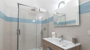 Une salle de bain moderne avec une douche à parois de verre, un meuble-lavabo doté d’un plan de travail en marbre et un miroir au-dessus du lavabo.
