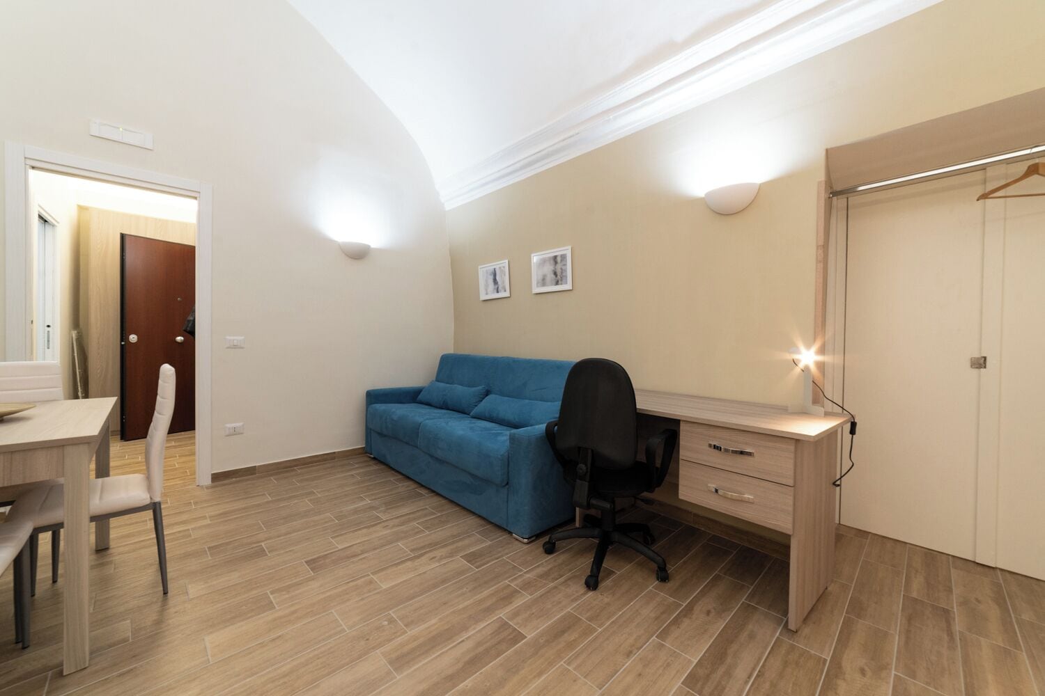 Une chambre à coucher de taille modeste, comprenant un bureau, un canapé bleu, une chaise et une armoire.