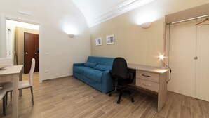 Une chambre à coucher de taille modeste, comprenant un bureau, un canapé bleu, une chaise et une armoire.