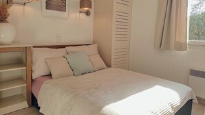 Ein Schlafzimmer mit einem Bett, zwei Wandlampen, einem Bild, einem Fenster mit Vorhängen und einer Heizung.