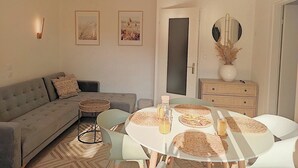 Ein Wohnzimmer mit einer Couch, einem Esstisch mit gewebten Untersetzern, einer Chandelüster und gerahmten Kunstwerken an der Wand.