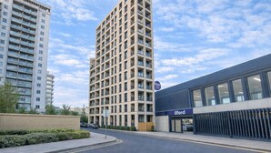 A modern building with a prominent entrance, a sign indicating a store, and a visible Ilford sign. - Skyline Views Apartment in the Heart of Ilford (Ilford)