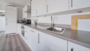 A modern kitchen with stainless steel appliances, white cabinetry, and a wooden cutting board. - Skyline Views Apartment in the Heart of Ilford (Ilford)