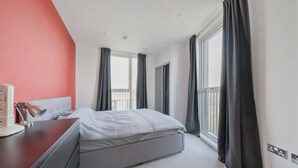 A modern bedroom with a bed, a desk, and a window with curtains. - Skyline Views Apartment in the Heart of Ilford (Ilford)