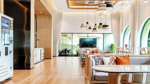A modern hotel lobby with a wooden floor, seating area with cushioned chairs, a large TV screen, and pendant lighting. - Title Legendary by Villacarte (Choeng Thale)