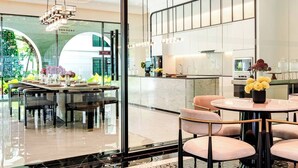 A modern dining area with a glass partition, a kitchen area, and a view of greenery outside. - Title Legendary by Villacarte (Choeng Thale)
