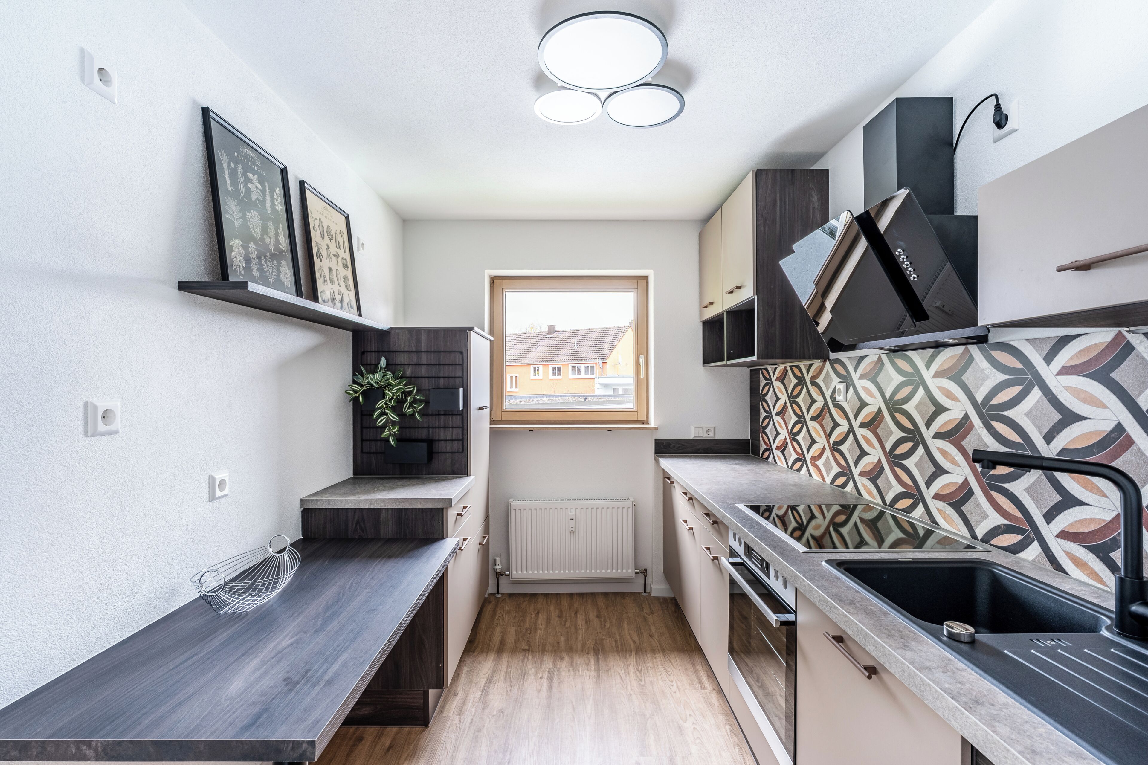 Een kleine keuken met een raam, ingebouwde apparatuur en een decoratieve spatbordenwand.