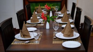 Una mesa de comedor con servilletas marrones, platos blancos y un florero con flores rojas.