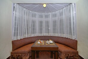 A room with a curved sofa, a small table with a tray of food, and sheer curtains. - Brij Villa Dalhousie A Colonial Luxury Retreat (Dalhousie)