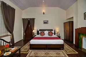 A hotel room with a large bed, a wooden headboard, a nightstand, a desk, a chair, a wardrobe, and a window with curtains. - Brij Villa Dalhousie A Colonial Luxury Retreat (Dalhousie)