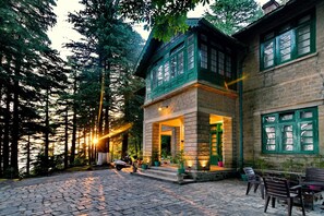 A building with a stone facade, green window frames, and a cobblestone courtyard. - Brij Villa Dalhousie A Colonial Luxury Retreat (Dalhousie)