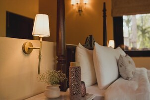 Un dormitorio con una lámpara de noche, una planta en maceta, jarrones decorativos y una cama con almohadas.