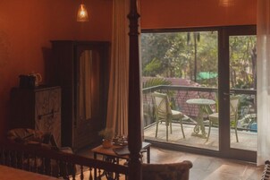 A room with a wooden staircase, a dining area with a table and chairs, and a view of a garden through a glass door.
