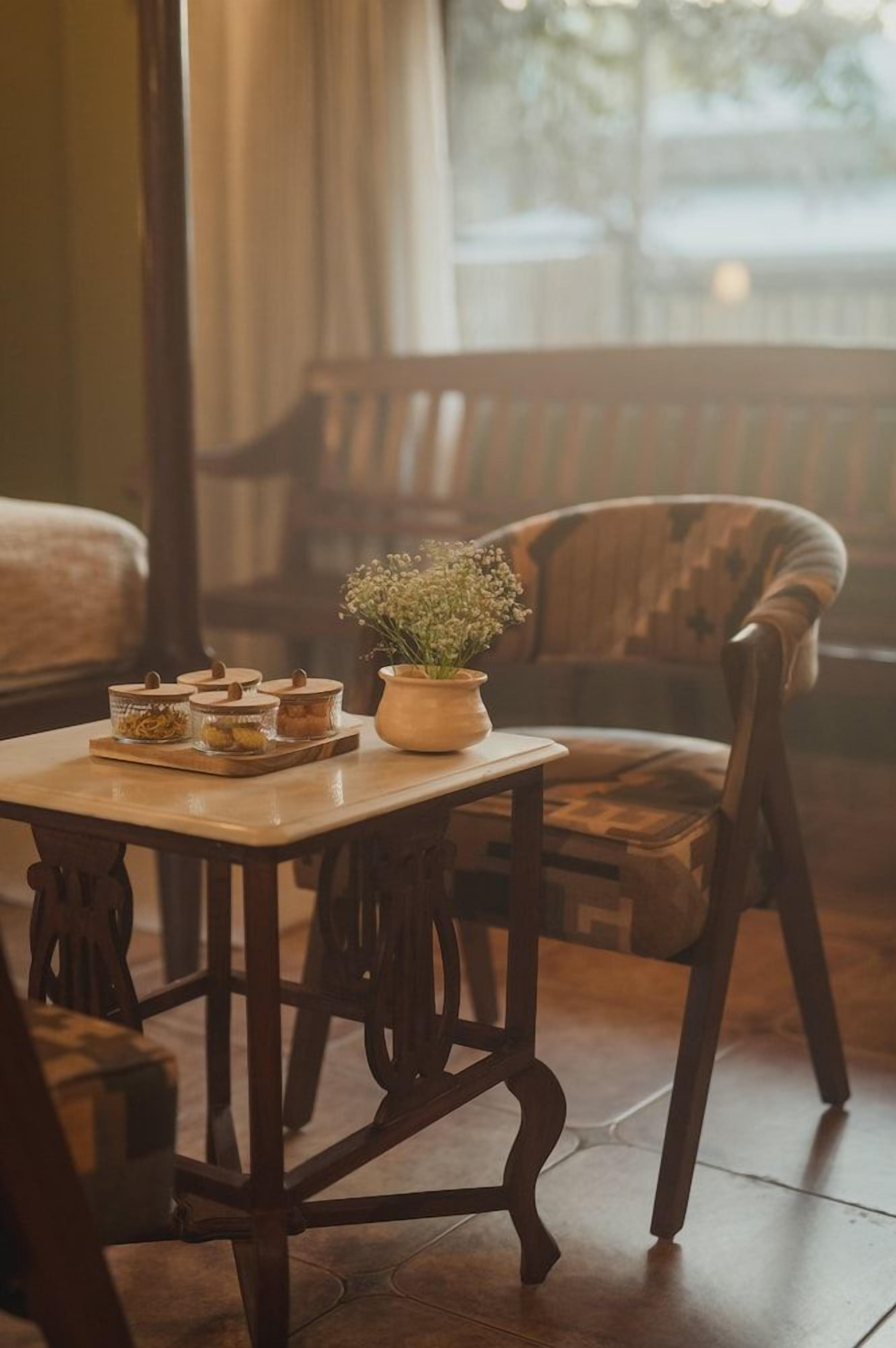 A wooden table with jars and a potted plant, a wooden chair, and a bench in a room with a window.
