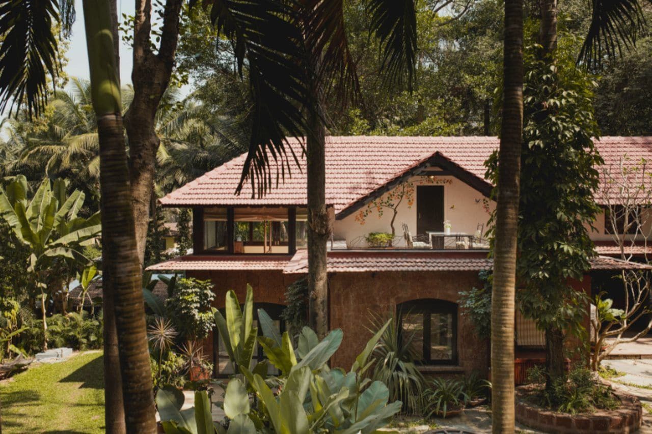 A two-story building with a tiled roof, surrounded by lush greenery and palm trees.