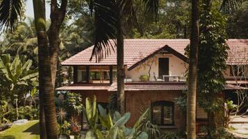 A two-story building with a tiled roof, surrounded by lush greenery and palm trees.