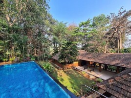 A swimming pool surrounded by lush greenery and a covered outdoor area with a tiled roof.