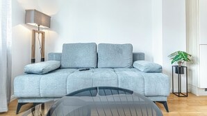 A light grey sofa with a remote control on it, a black table in front, and a tall floor lamp beside the sofa. - Chic 1BR with 1LV Apt In Central Vienna (Vienna)