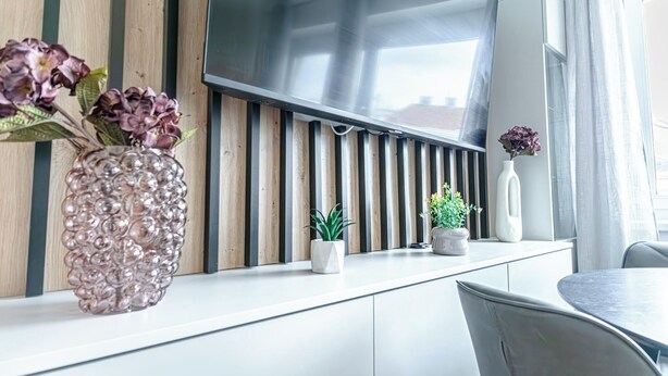 A modern interior with a flat-screen TV mounted on a wall, a dining area with a round table, and potted plants on a counter. - Chic 1BR with 1LV Apt In Central Vienna (Vienna)