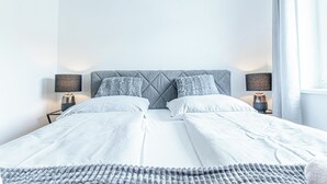 A neatly made double bed with a grey headboard, two bedside lamps, and a grey knitted throw. - Chic 1BR with 1LV Apt In Central Vienna (Vienna)