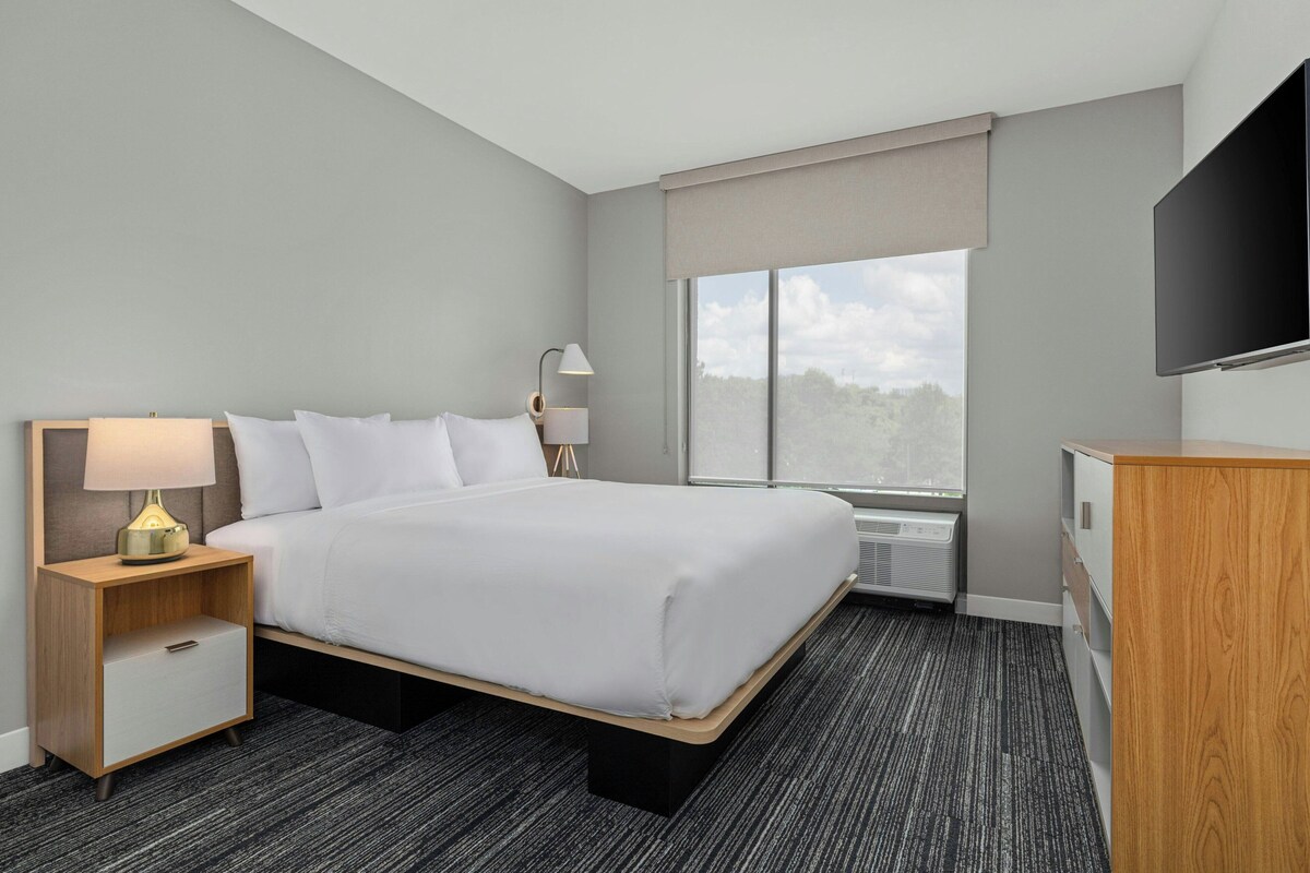 A hotel room with a bed, bedside tables, a lamp, a TV, and a window with a view.