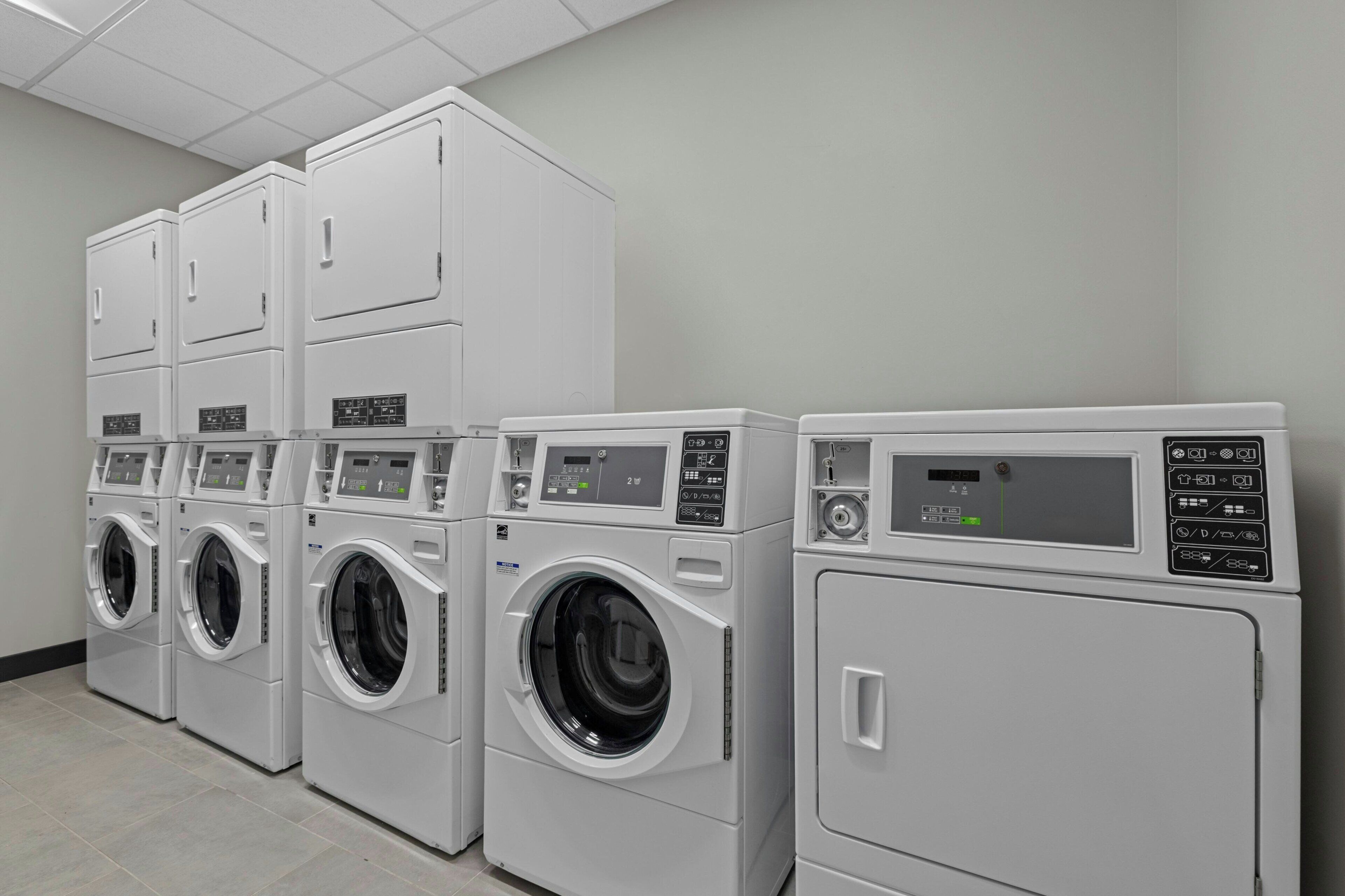 A row of stacked, modern, white laundry machines in a commercial setting.