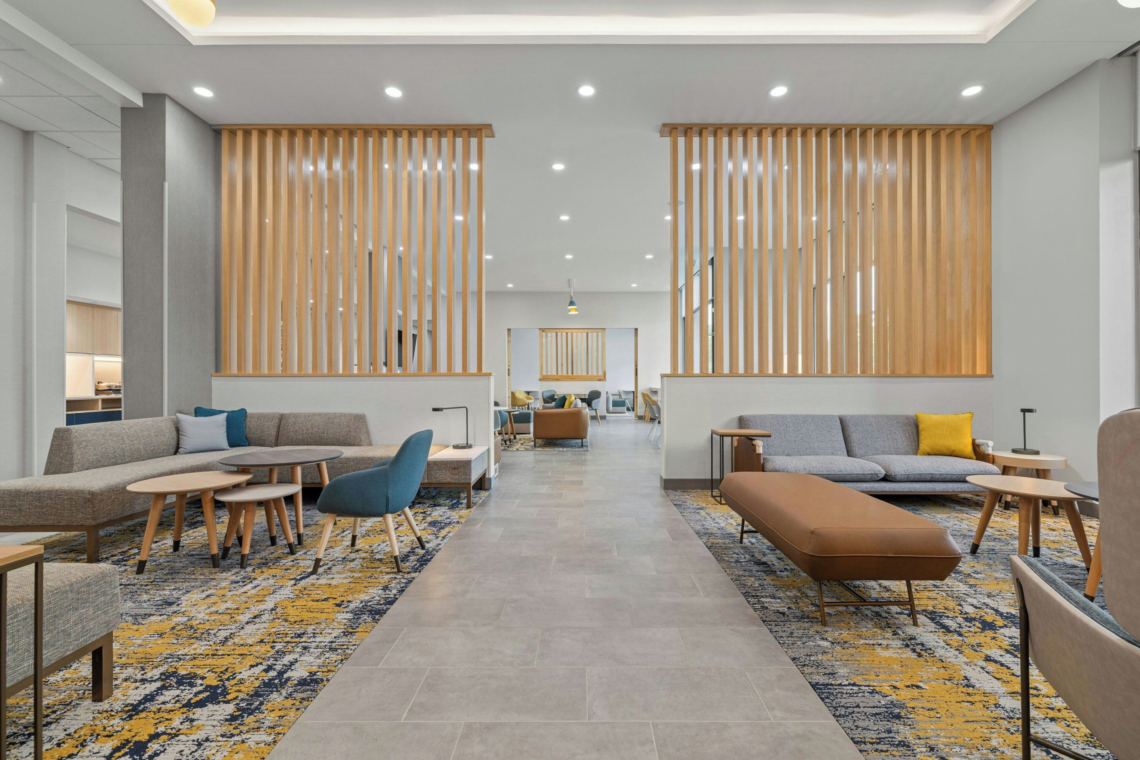 Een moderne hotelentree met een centraal zithoek, houten scheidingswanden en een kamerbreed tapijt met dessin.