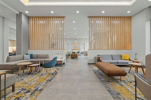 Un moderno vestíbulo de hotel con una zona de estar central, separadores de madera y una alfombra estampada.