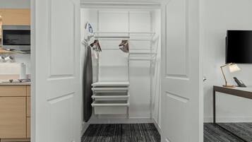 A hotel room with a walk-in closet, a desk with a lamp, and a flat-screen TV.