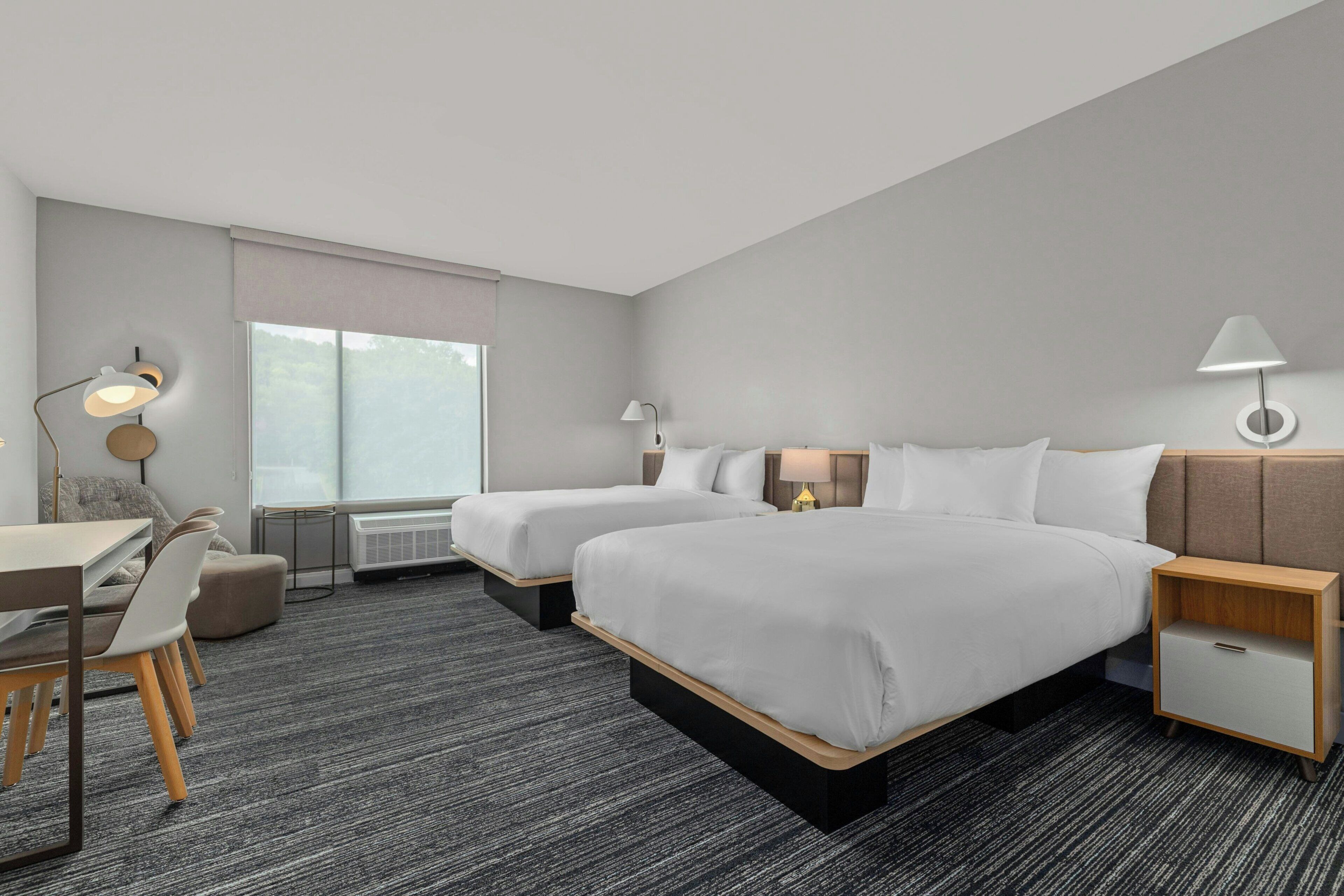Een hotelkamer met twee bedden, een bureau, een stoel en een raam met uitzicht.