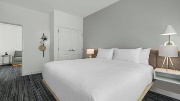 A hotel room with a large bed, a bedside table with a lamp, a chair, and a door.