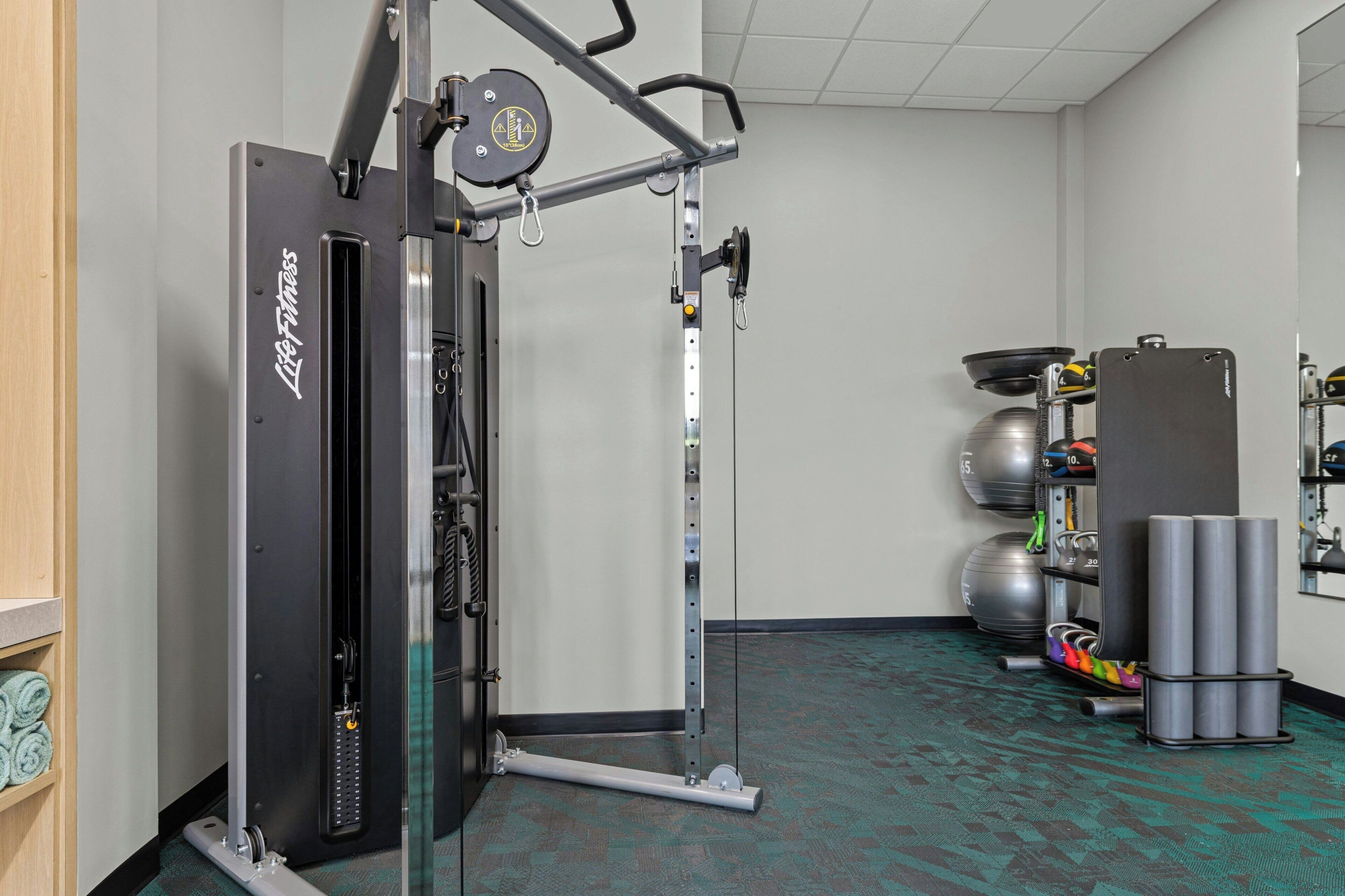 A gym with a cable machine, exercise balls, and a weight rack.