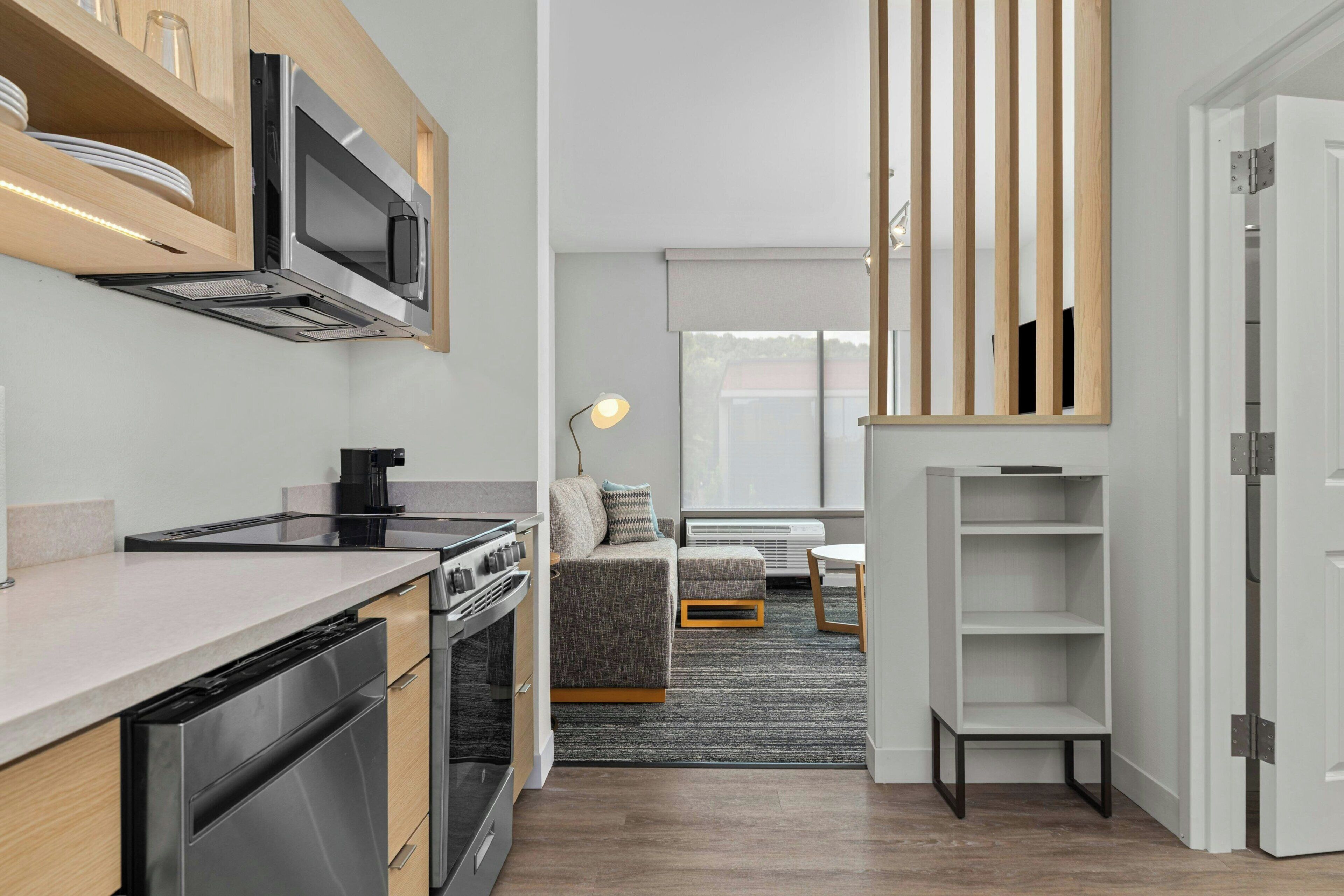 A modern kitchen with stainless steel appliances, a dining area with a sofa and table, and a view of the outdoors through large windows.