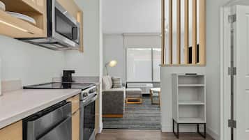 A modern kitchen with stainless steel appliances, a dining area with a sofa and table, and a view of the outdoors through large windows.