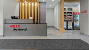 Balcão de recepção com placa indicando 'HELLO Brentwood', um registrador de caixa e um telefone fixado na parede.