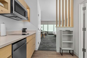 A modern kitchen with a microwave, coffee machine, and dishwasher. There is a dining area with a table and chairs, and a view of the outside through large windows.