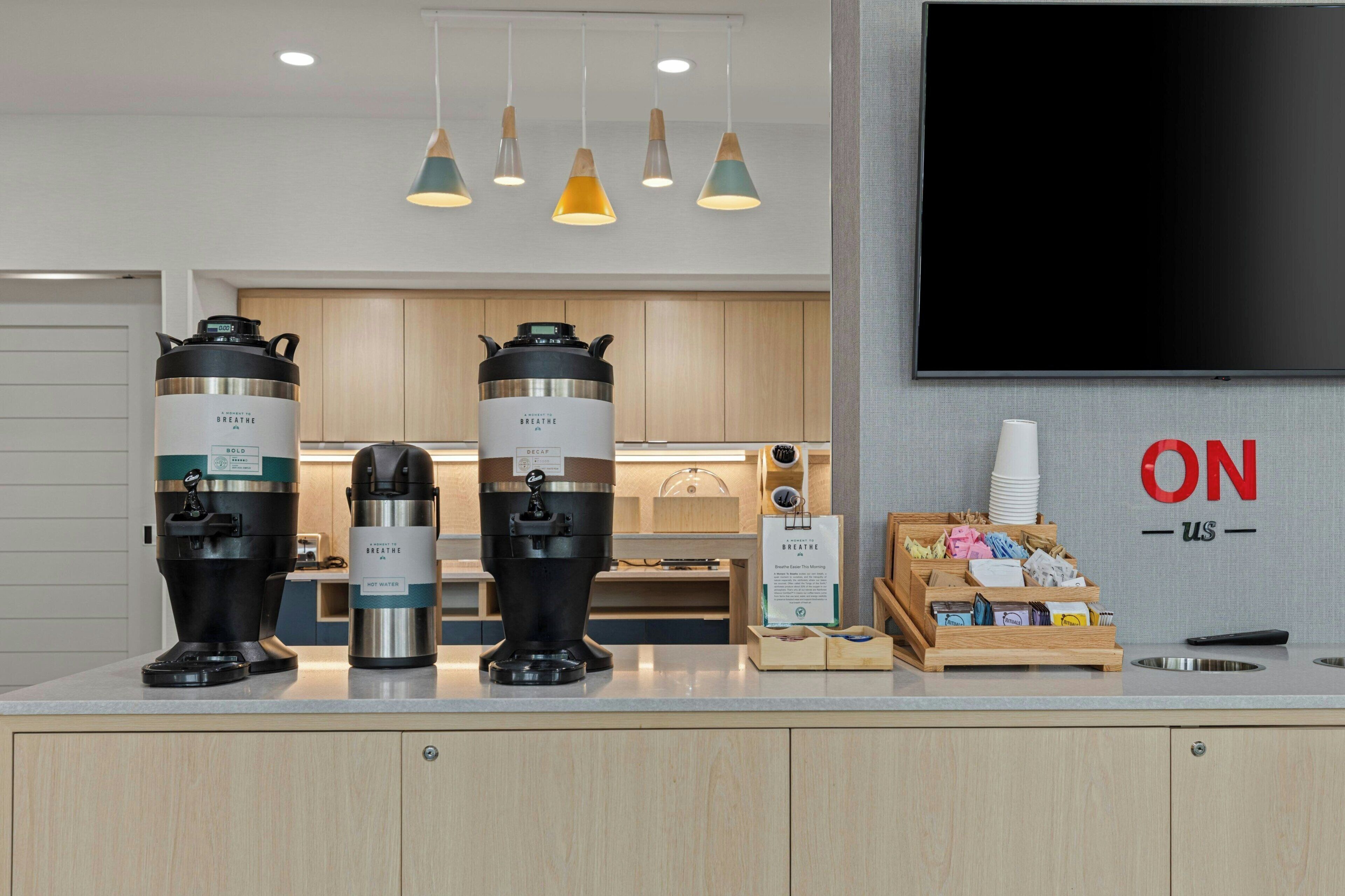 Ein moderner Küchenbereich mit drei Wasserspendern, einer Kaffeemaschine und einer Theke mit einer Kaffeestation.