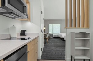 Habitación de hotel moderna con kitchenette, cama, escritorio y vista al exterior.