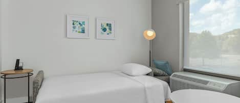 Ett hotellrum med en säng, ett runt bord, en golvlampa och två inramade konstverk på väggen.